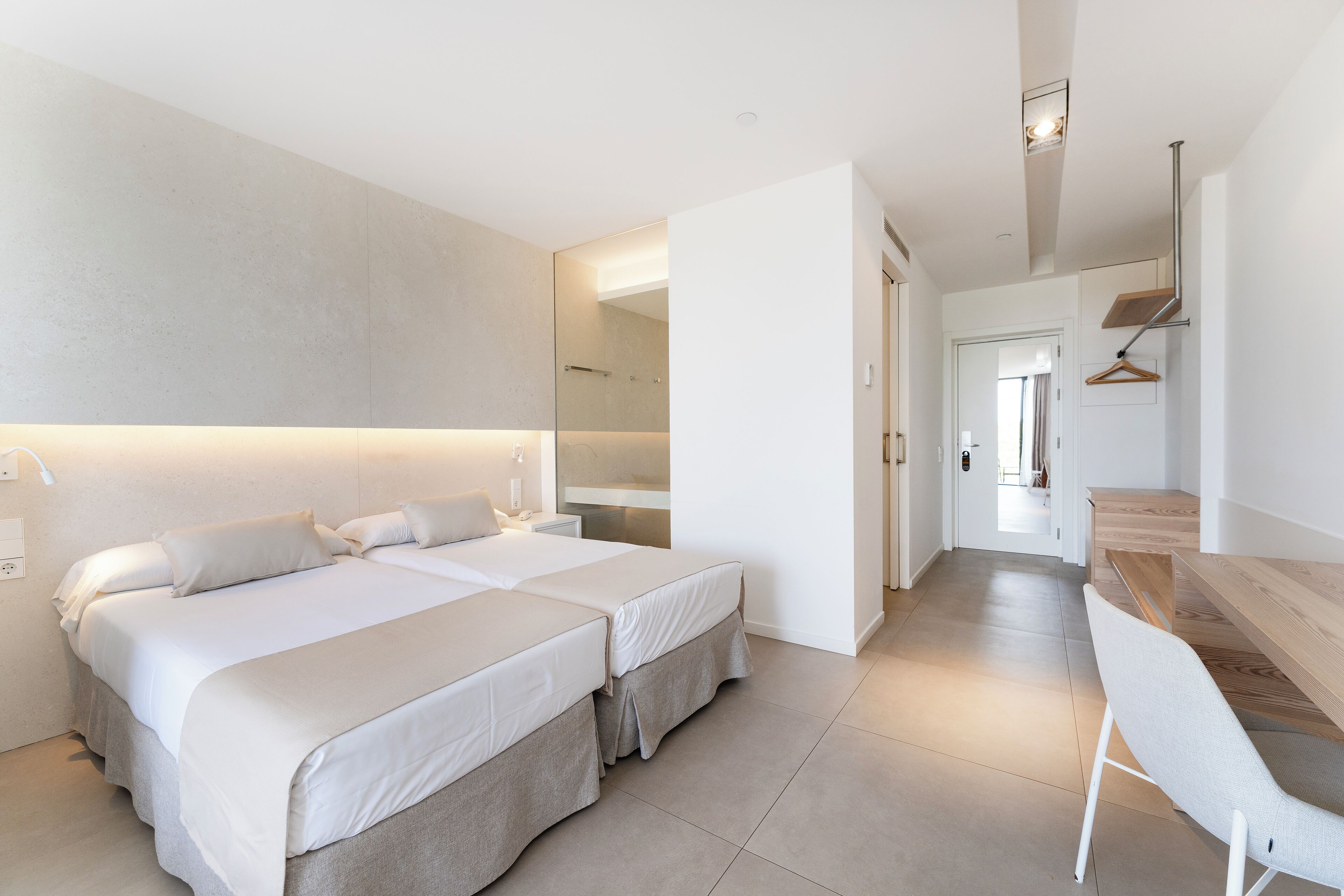 A modern hotel room with two beds, a wooden desk, and a mirror.