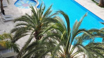 A large rectangular swimming pool with a blue center, surrounded by lounge chairs and palm trees.