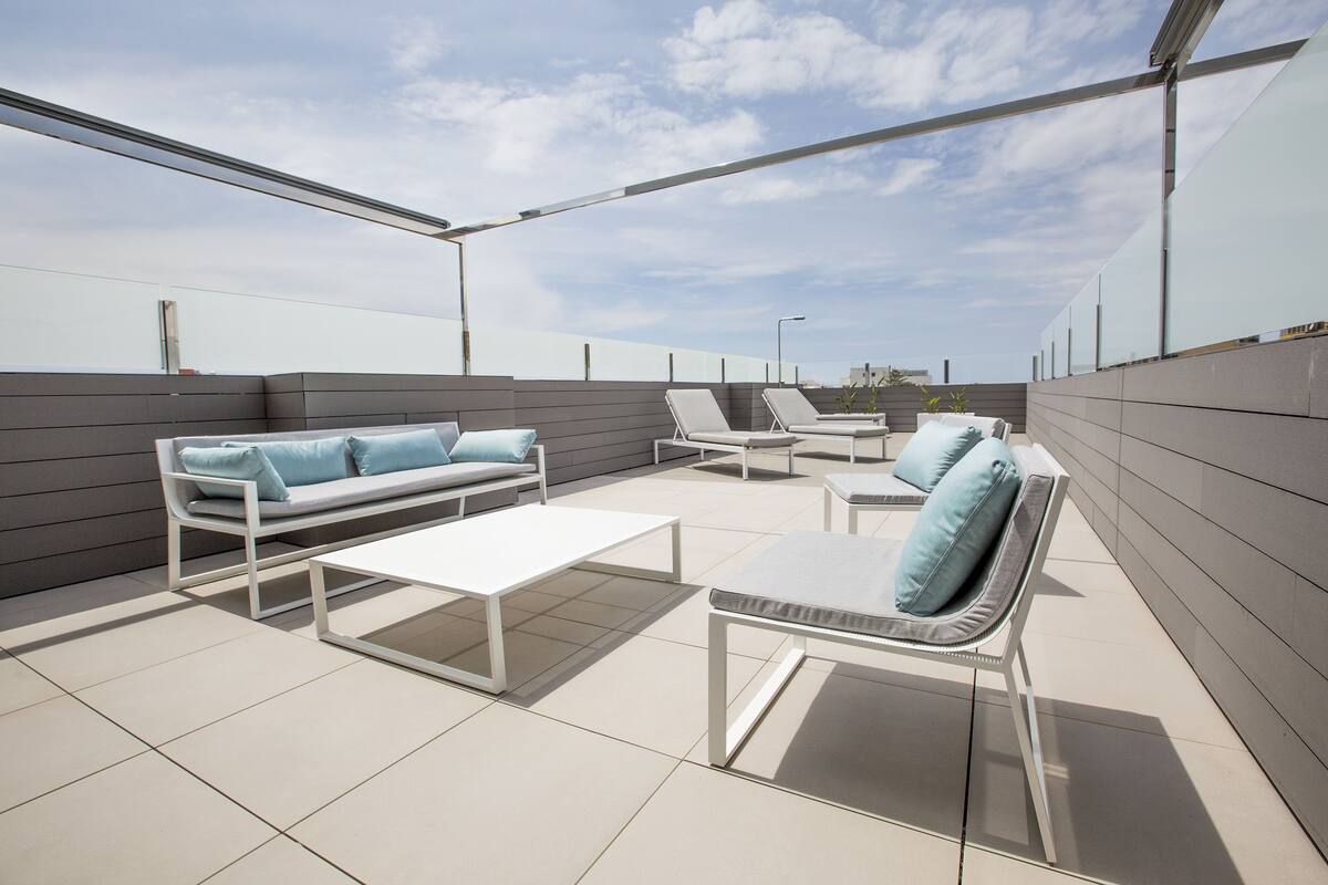 A rooftop terrace with a sofa, chairs, and a table.