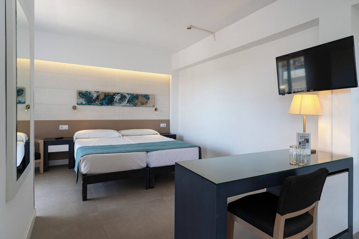 A hotel room with a bed, a desk, a chair, a TV, and a lamp.