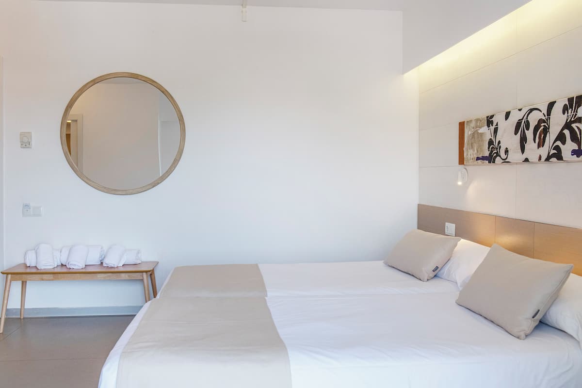 A hotel room with a large bed, a round mirror, a bench with towels, and a wall-mounted artwork.
