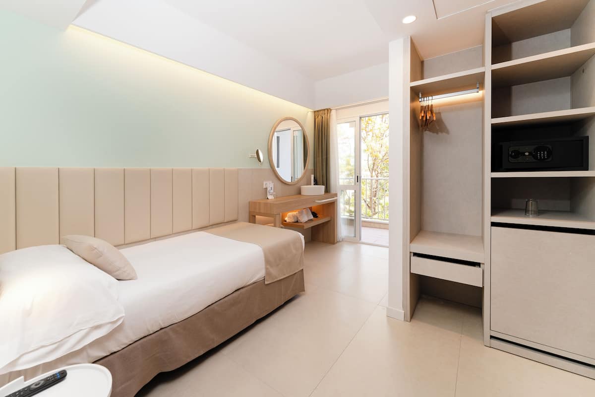 A modern hotel room with a bed, bedside table, mirror, and built-in wardrobe.