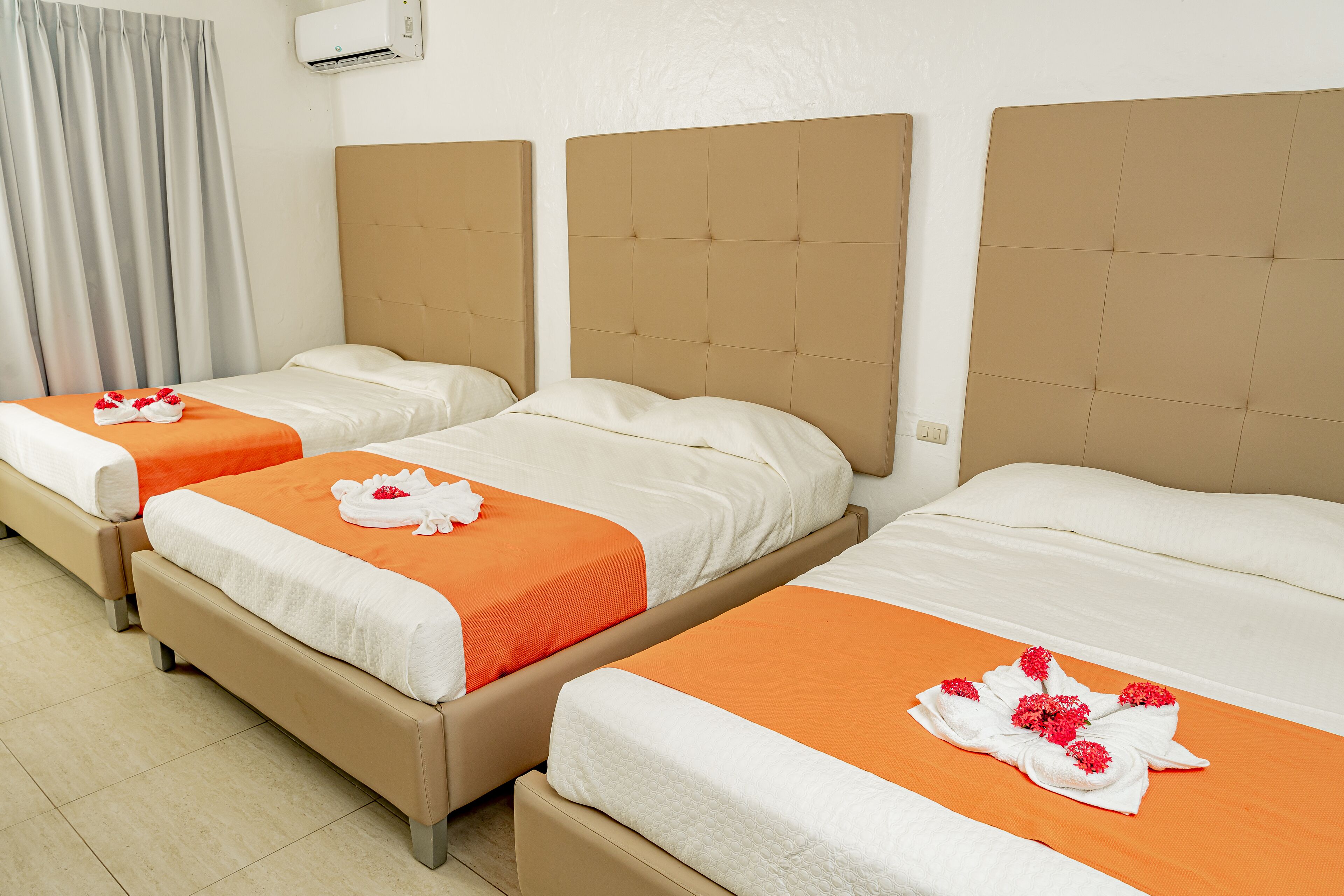 A hotel room with three beds, each with a beige headboard and orange bedspread.