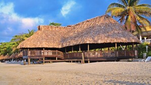 A beachside structure with a thatched roof, wooden deck, and lounge chairs. - Hotel Palma Real (Jutiapa)
