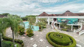 Surrounded by lush greenery and palm trees, this resort features a central pool, a vibrant mural, and a beautifully maintained garden with a circular hedge design.