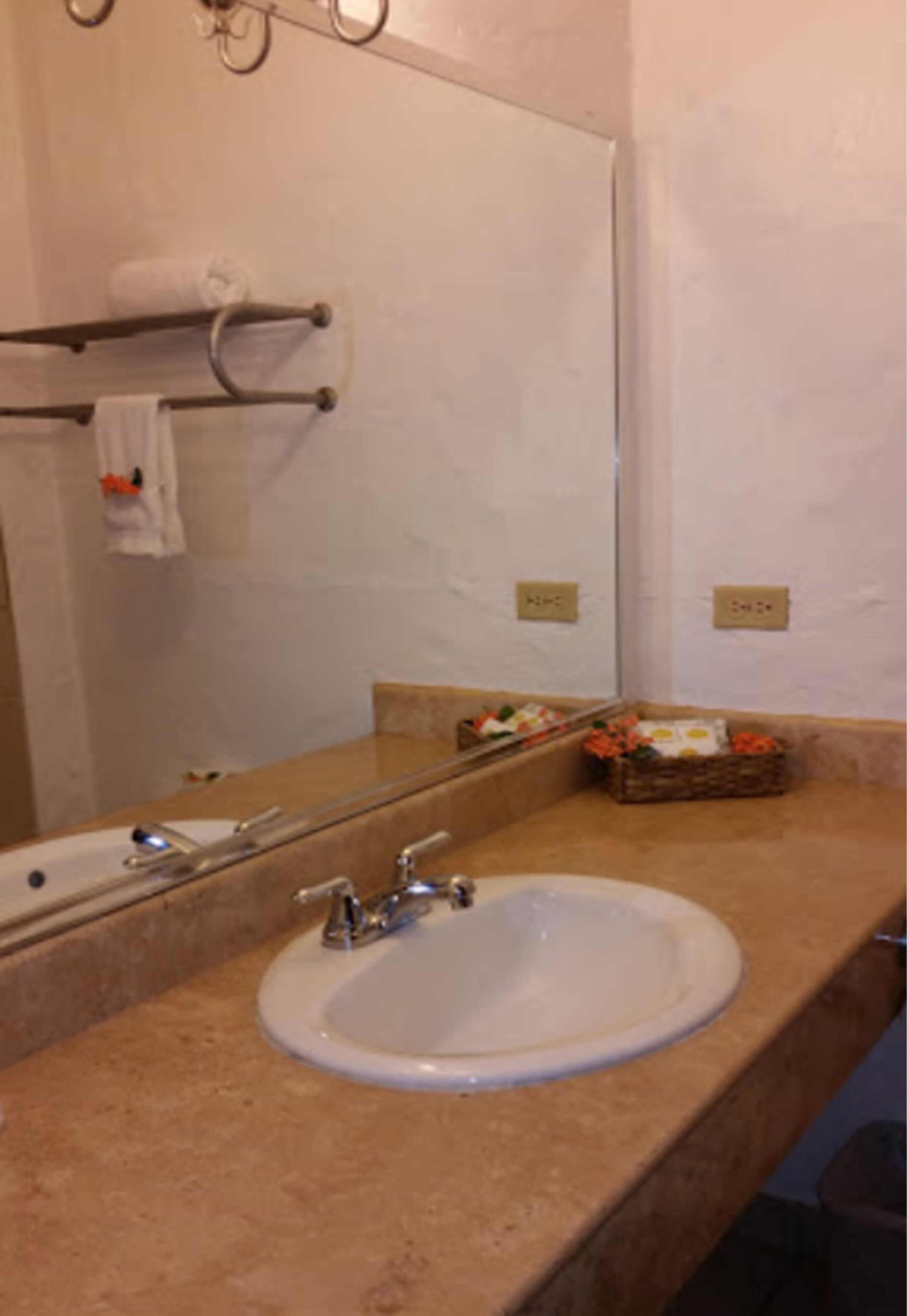 Een badkamer met een wastafel, spiegel, handdoekhouder en een klein mandje met toiletartikelen.