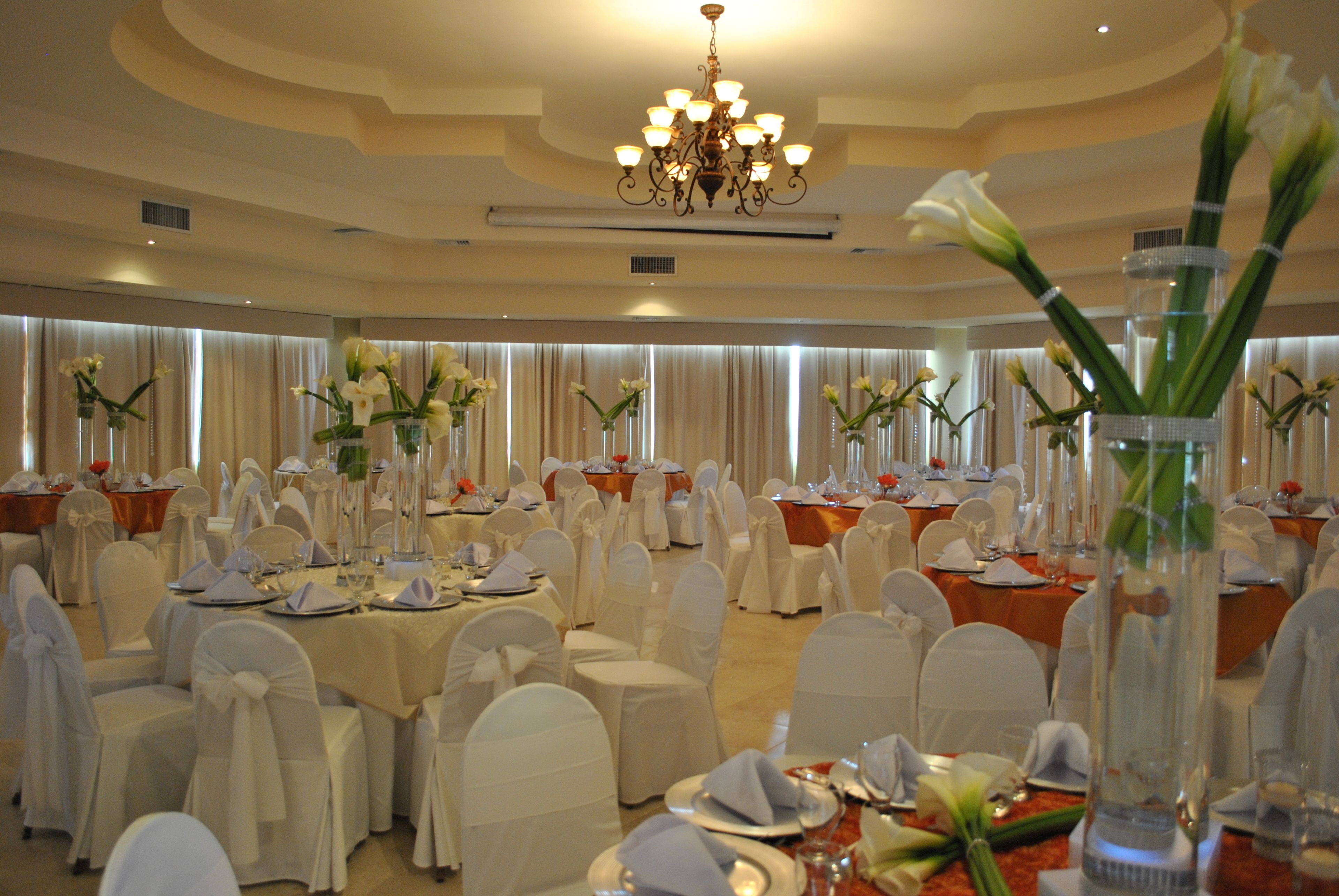 Un salón de banquetes con mesas redondas, sillas blancas y centros de mesa florales.