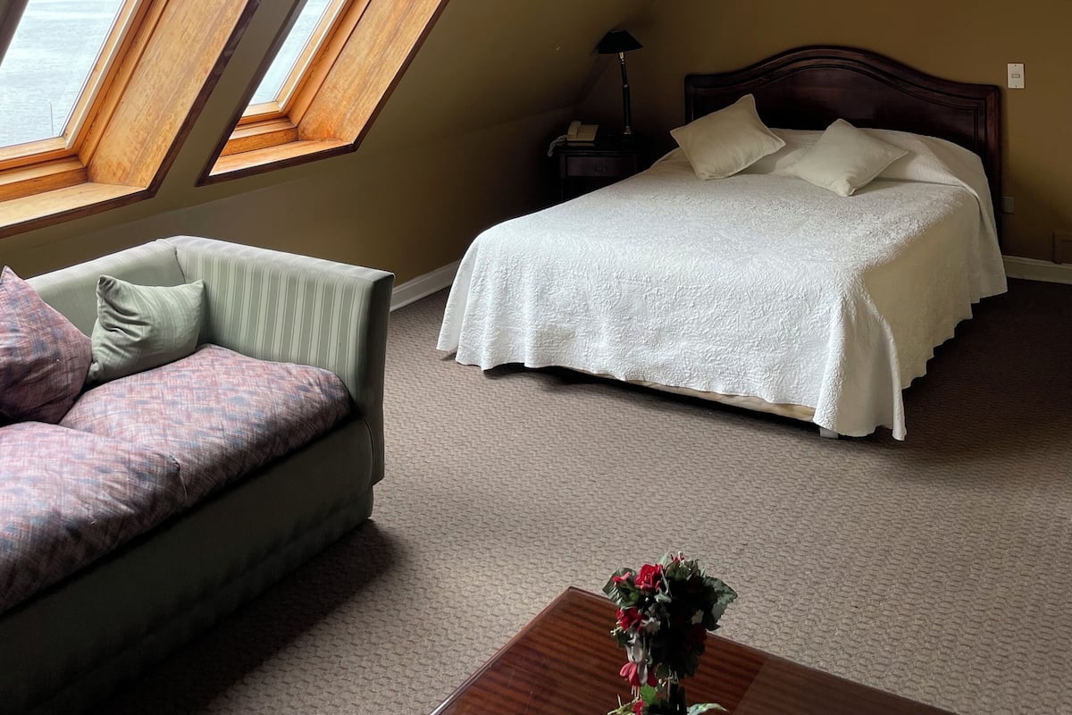 A bedroom with a bed, a chair, a nightstand, and a window with a view.