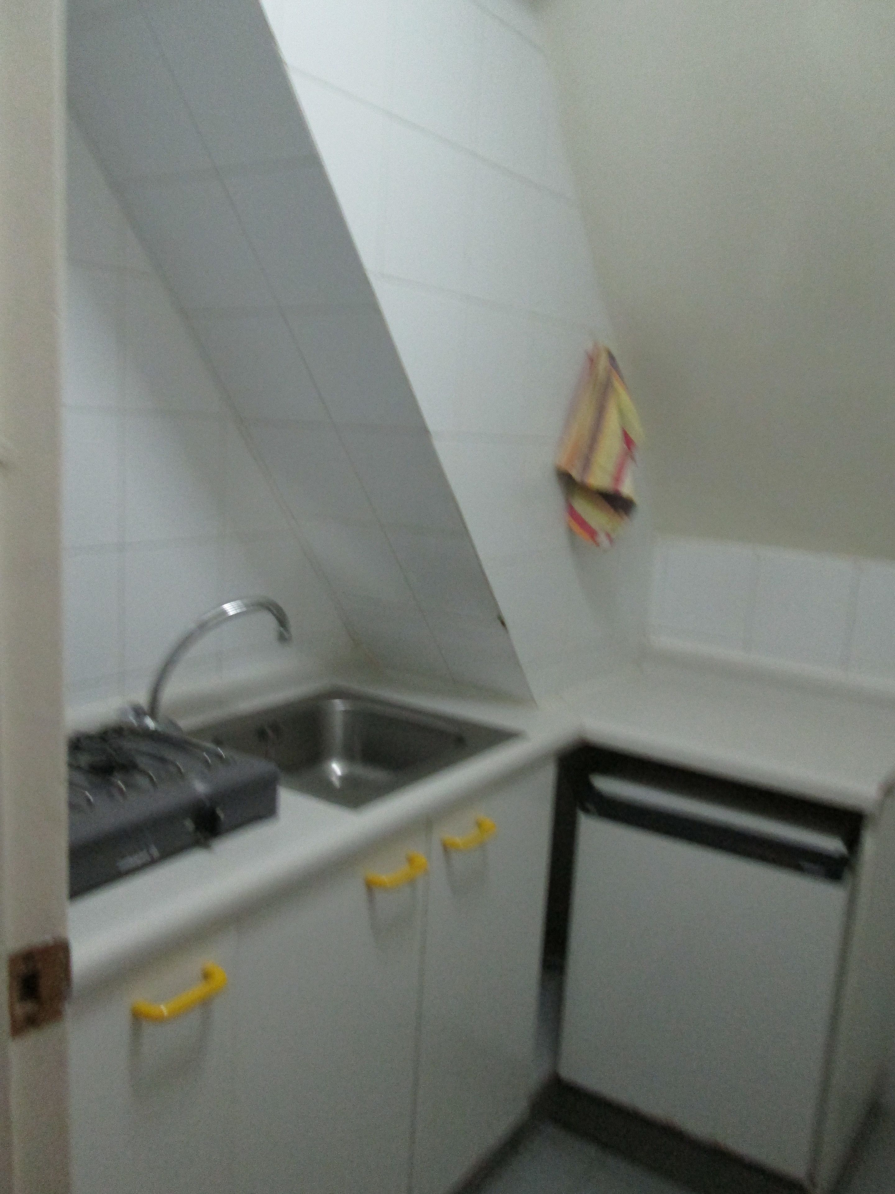 Uma cozinha pequena com pia, fogão e armários com puxadores amarelos.