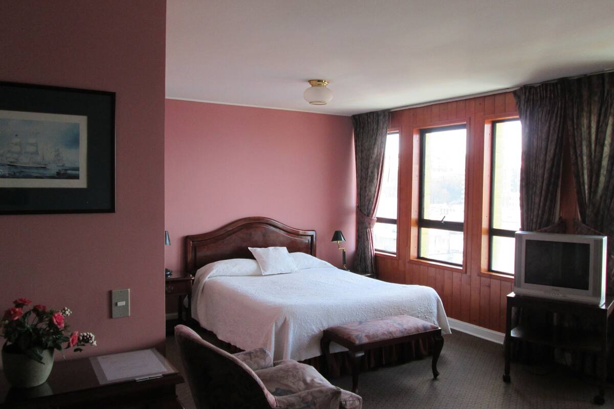 A hotel room with a large bed, a desk with a chair, a television, and a window with curtains.