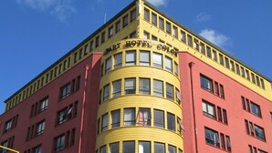 A corner building with a curved yellow facade and a red base. - Apart Hotel Colon (Puerto Montt)