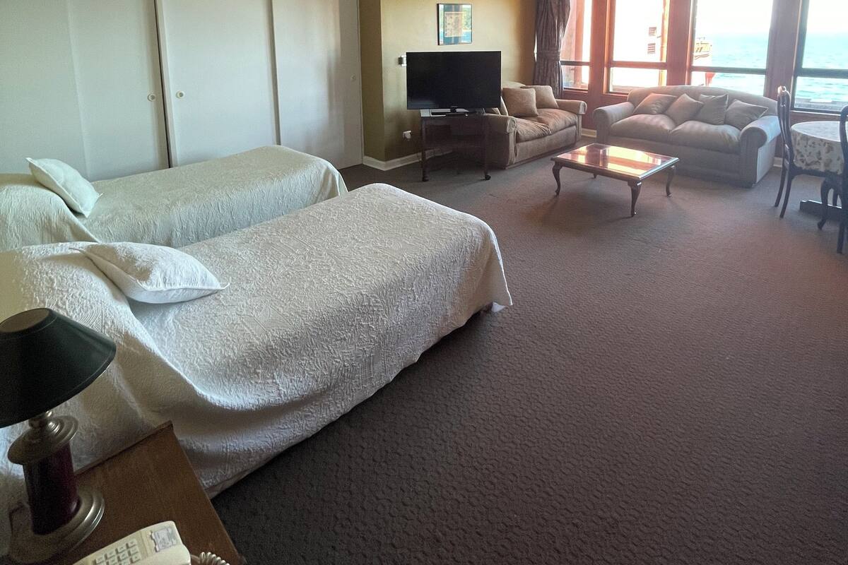 A hotel room with two beds, a TV, a sofa, and a view of the sea.