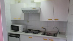 A compact kitchen with white cabinets, a microwave, a gas stove, and a sink. - Apart Hotel Colon (Puerto Montt)