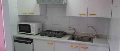 Una cocina compacta con armarios blancos, un microondas, una cocina a gas y un lavamanos.