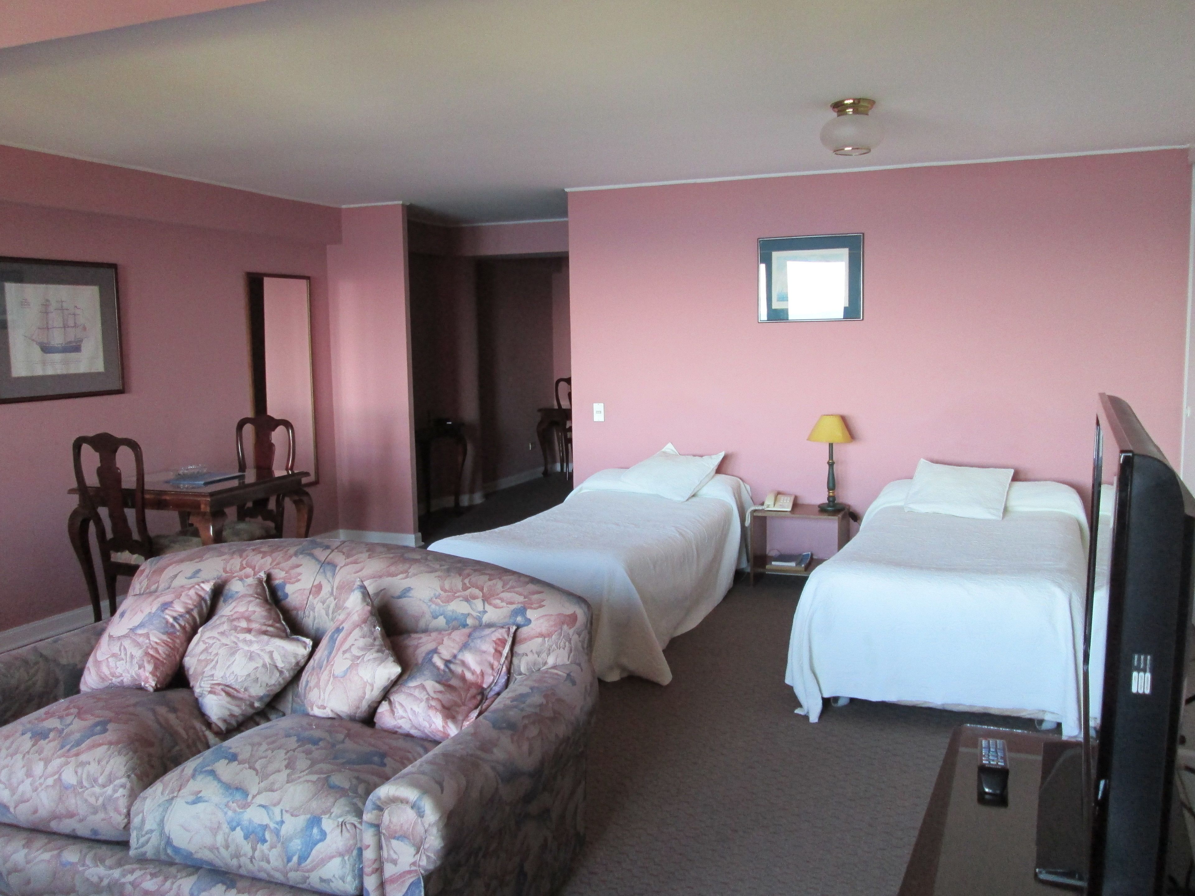 A hotel room with two beds, a sofa, a desk, and a television.