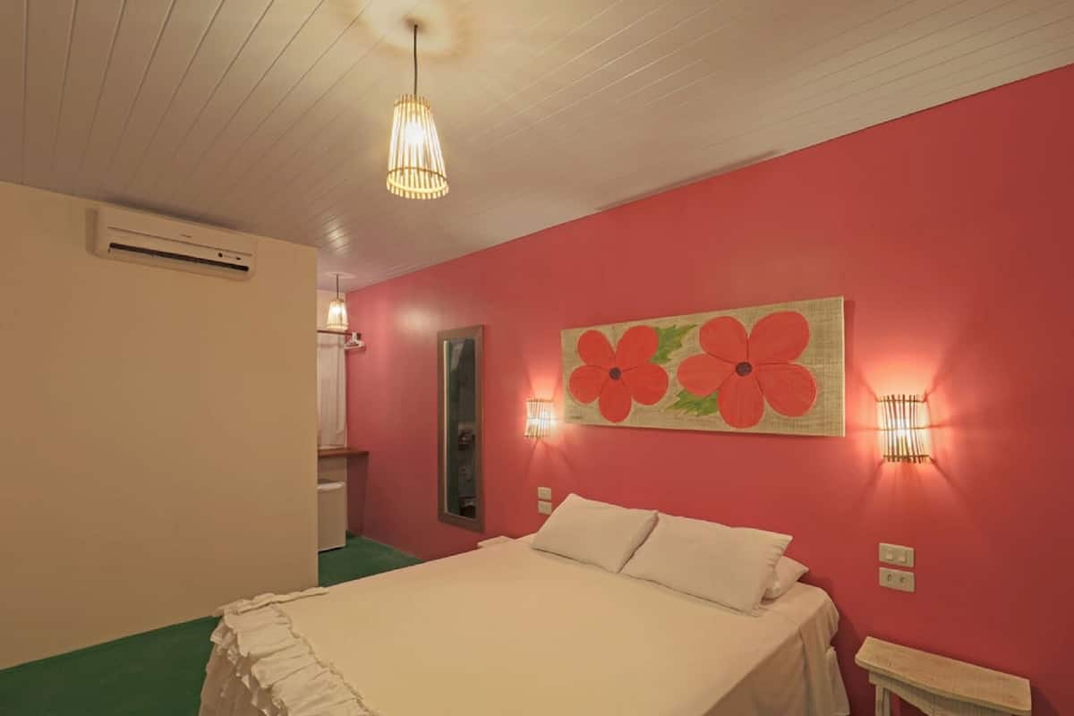 A bedroom with a bed, a mirror, and a wall-mounted flower painting.