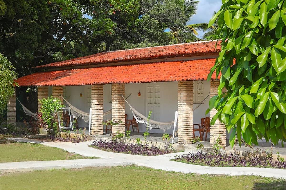 A building with a red-tiled roof, brick walls, and a covered porch with hammocks.