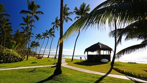 Escena en la playa con una cabaña de techo de paja, palmeras y una vista despejada del océano.