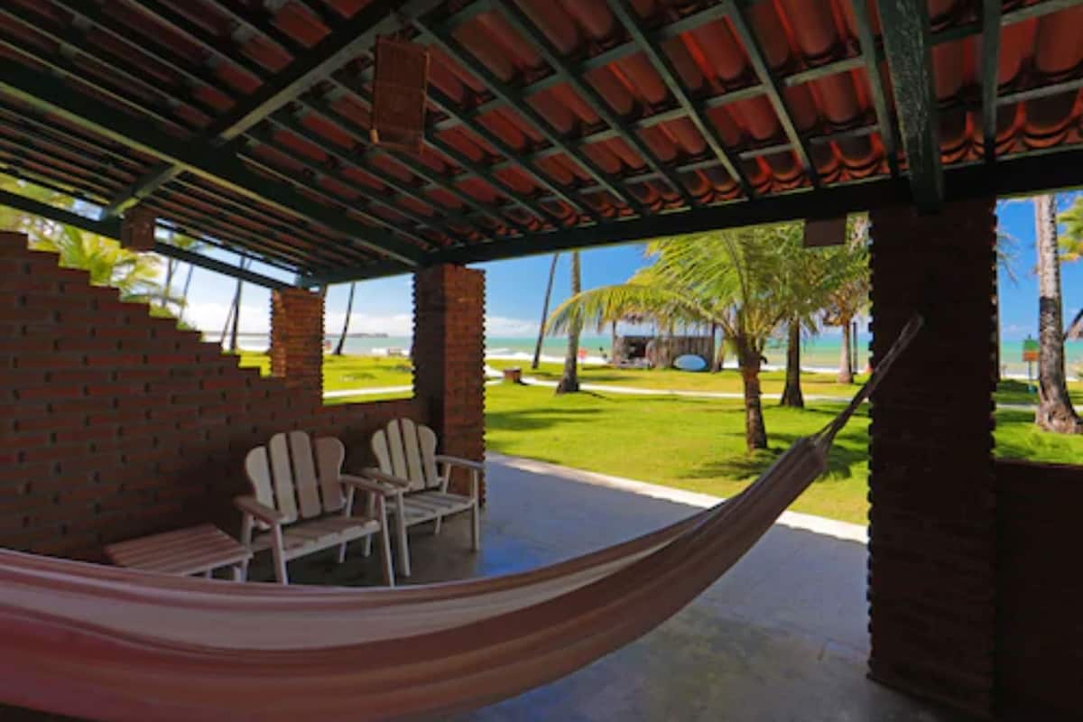 A covered outdoor seating area with a hammock, brick walls, and a view of the beach.