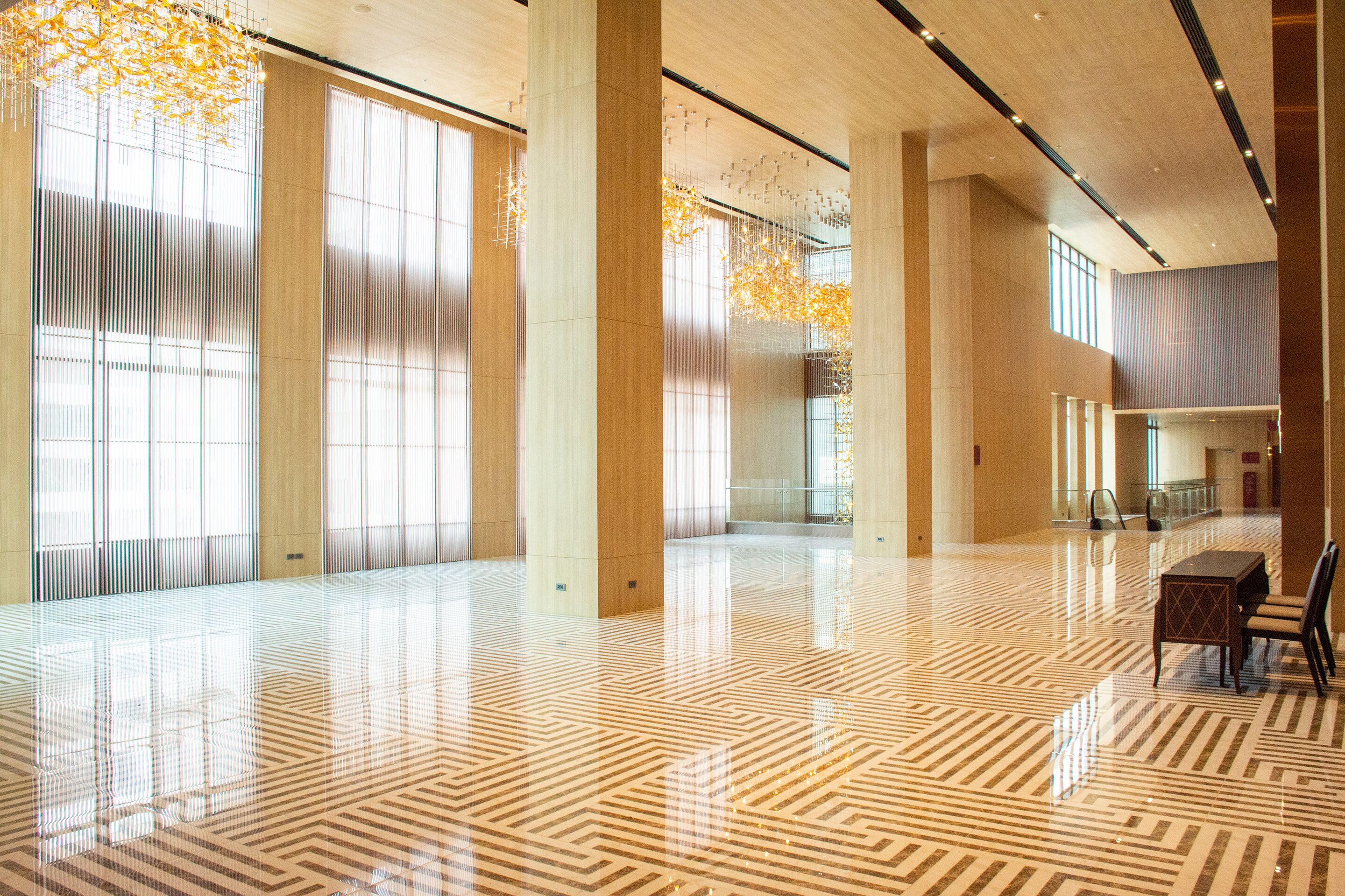 A spacious lobby with a patterned floor, large windows, and a modern chandelier.