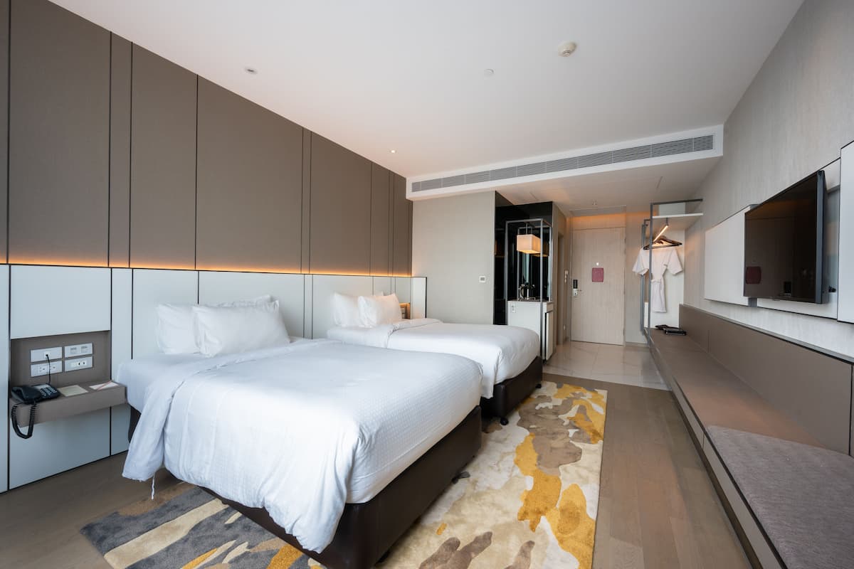 A modern hotel room with a large bed, bedside tables, a TV, and a bathroom with a mirror and towel rack.
