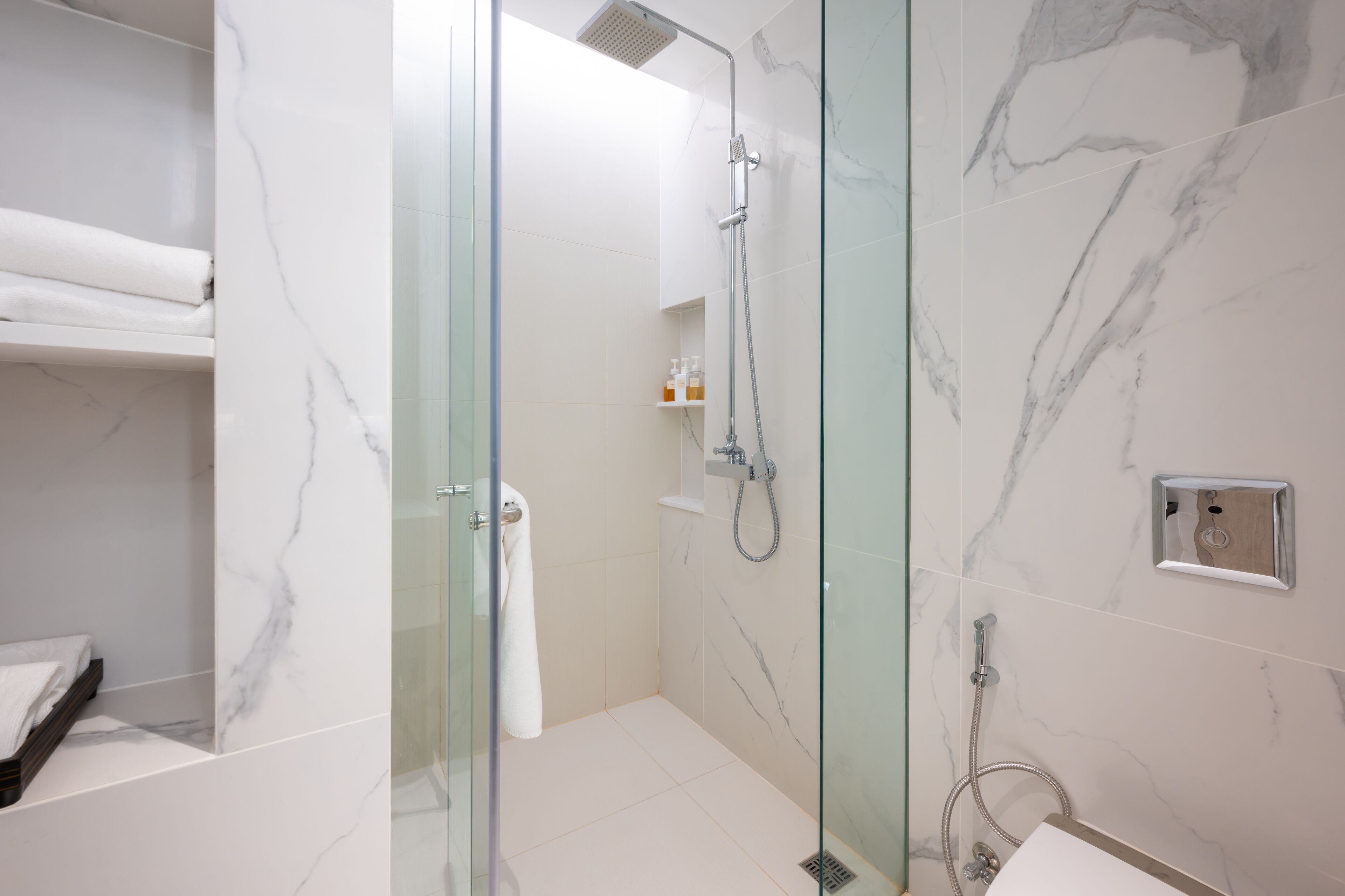 A modern bathroom with a glass shower enclosure, marble walls, and a white sink.