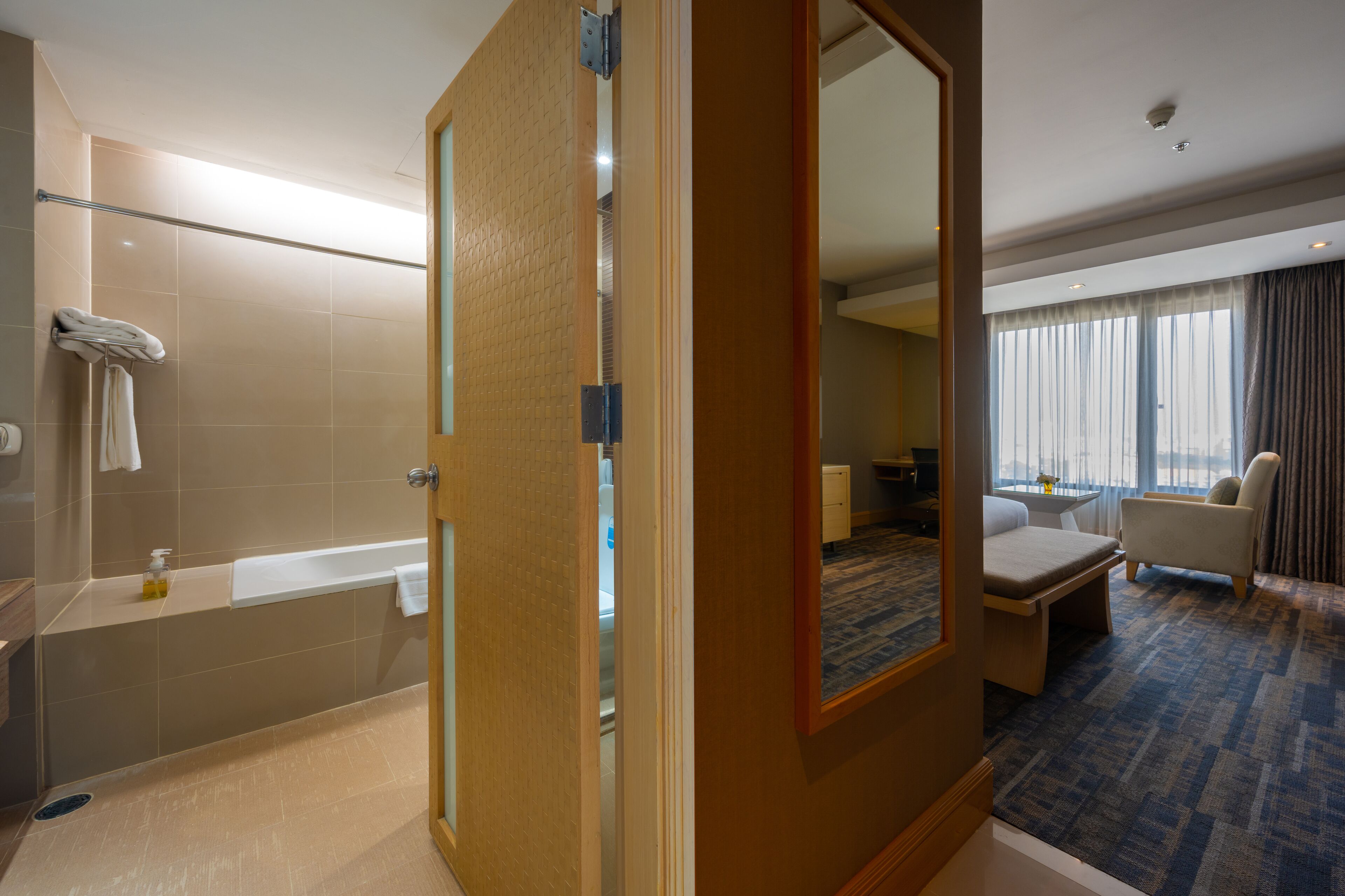 Une chambre d’hôtel dotée d’une baignoire, d’un coin salon avec une table et des chaises, et d’une grande fenêtre avec des rideaux.