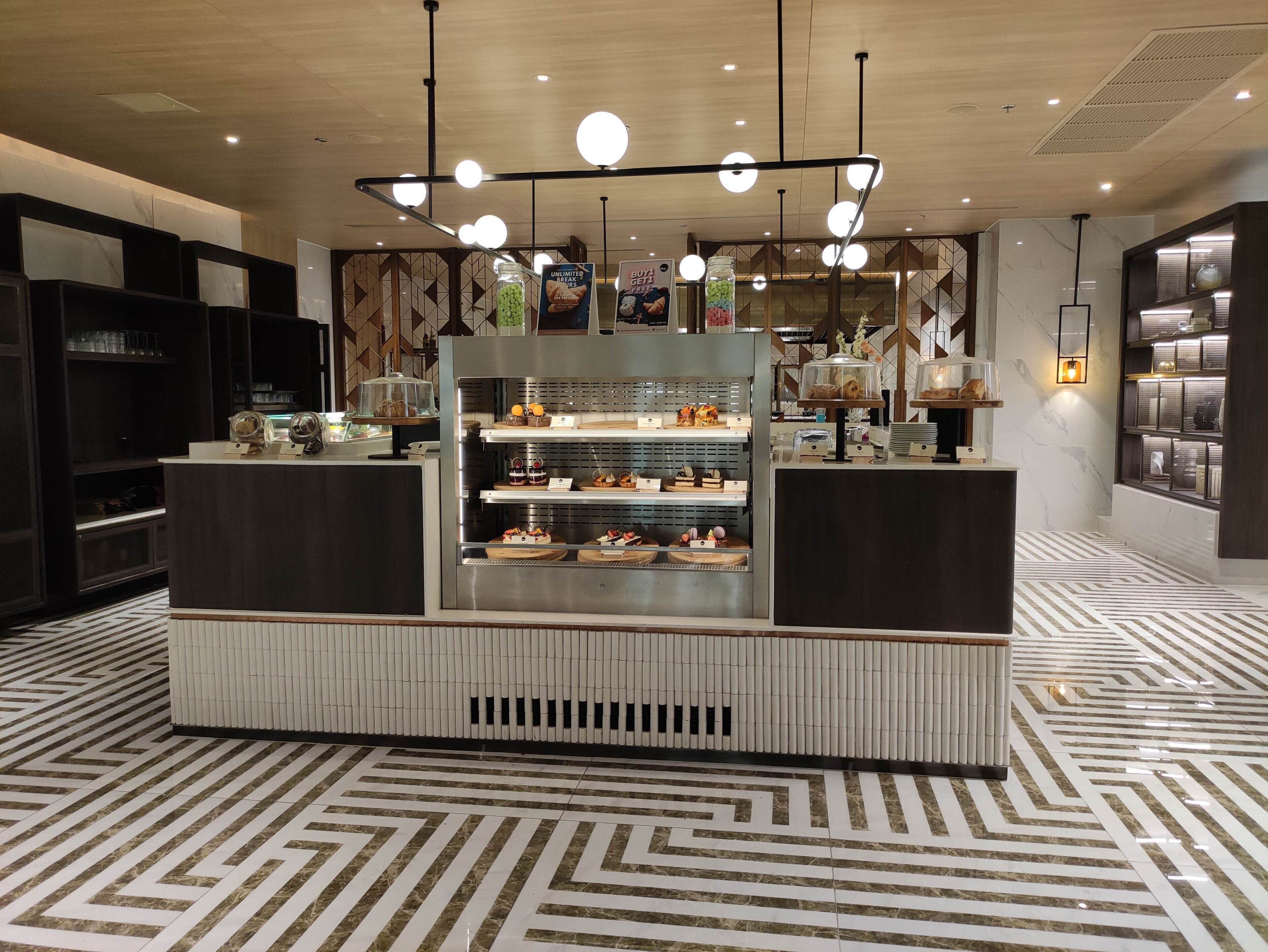 Een modern café met een vloer van marmerlook, een centrale vitrine voor desserts en hanglampen.