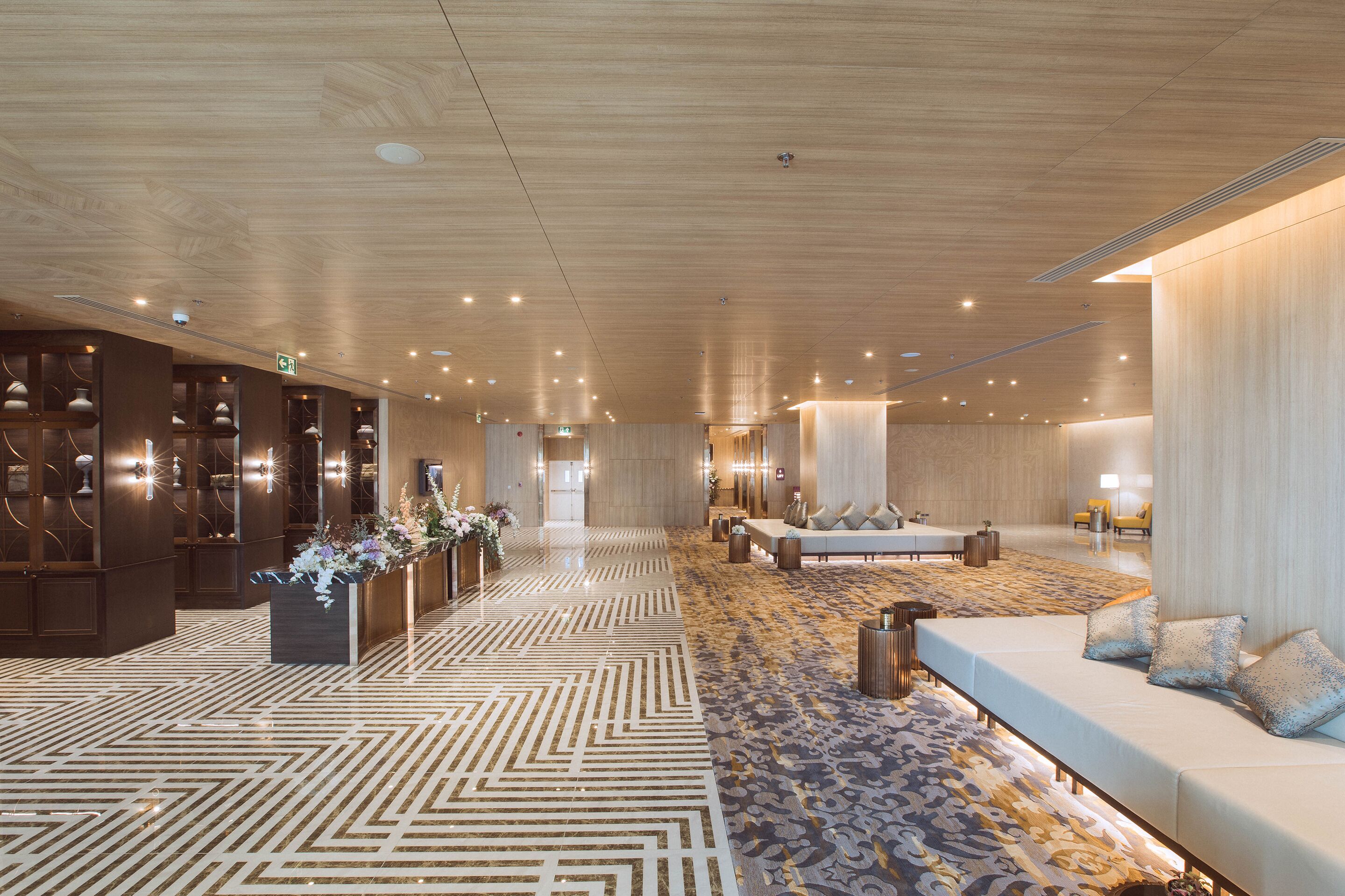 A spacious lobby with a patterned floor, a reception desk, seating area, and a large wall with a light fixture.