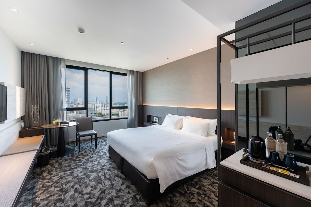 A modern hotel room with a large bed, a desk, a chair, and a view of the city.