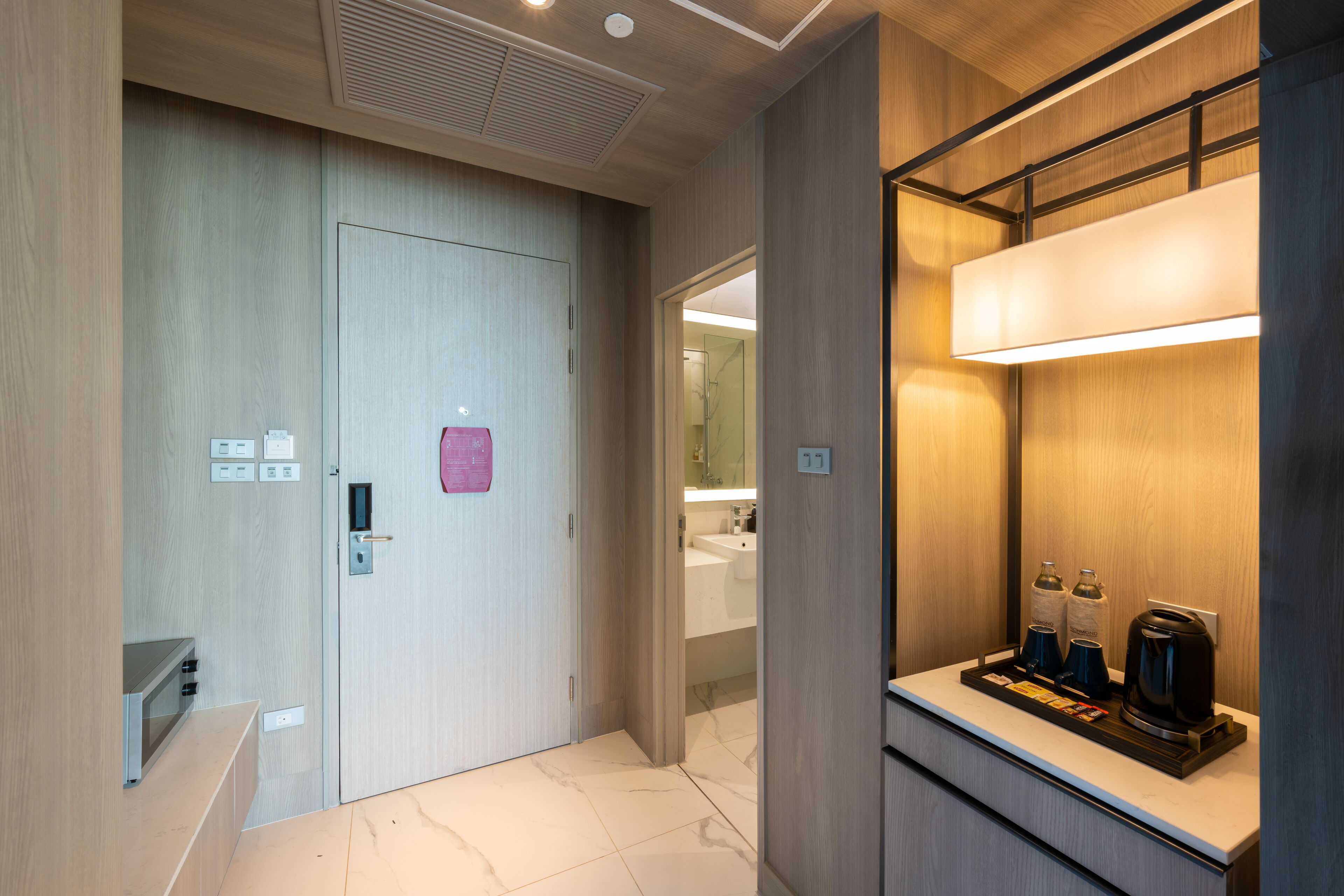 A modern hotel room with a wooden floor, a built-in microwave, a coffee maker, and a small tray with amenities.
