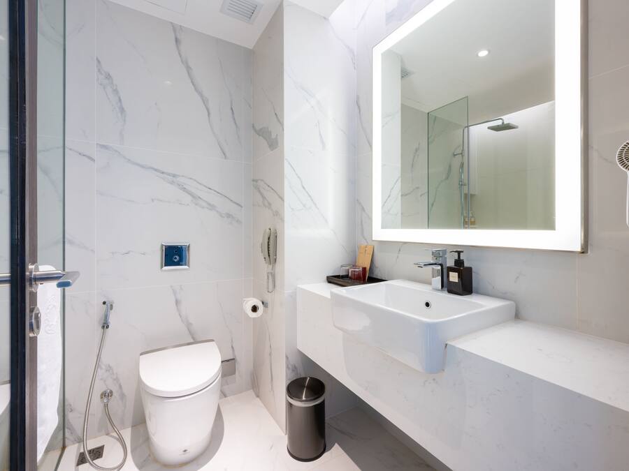 Un baño moderno con cabina de ducha de vidrio, inodoro blanco, lavamanos con espejo y cubo de basura.