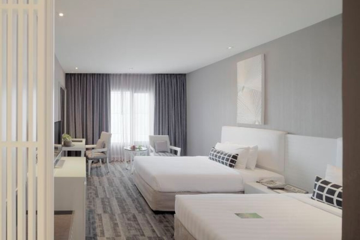 Een hotelkamer met twee bedden, een bureau, een stoel en uitzicht op de omgeving.