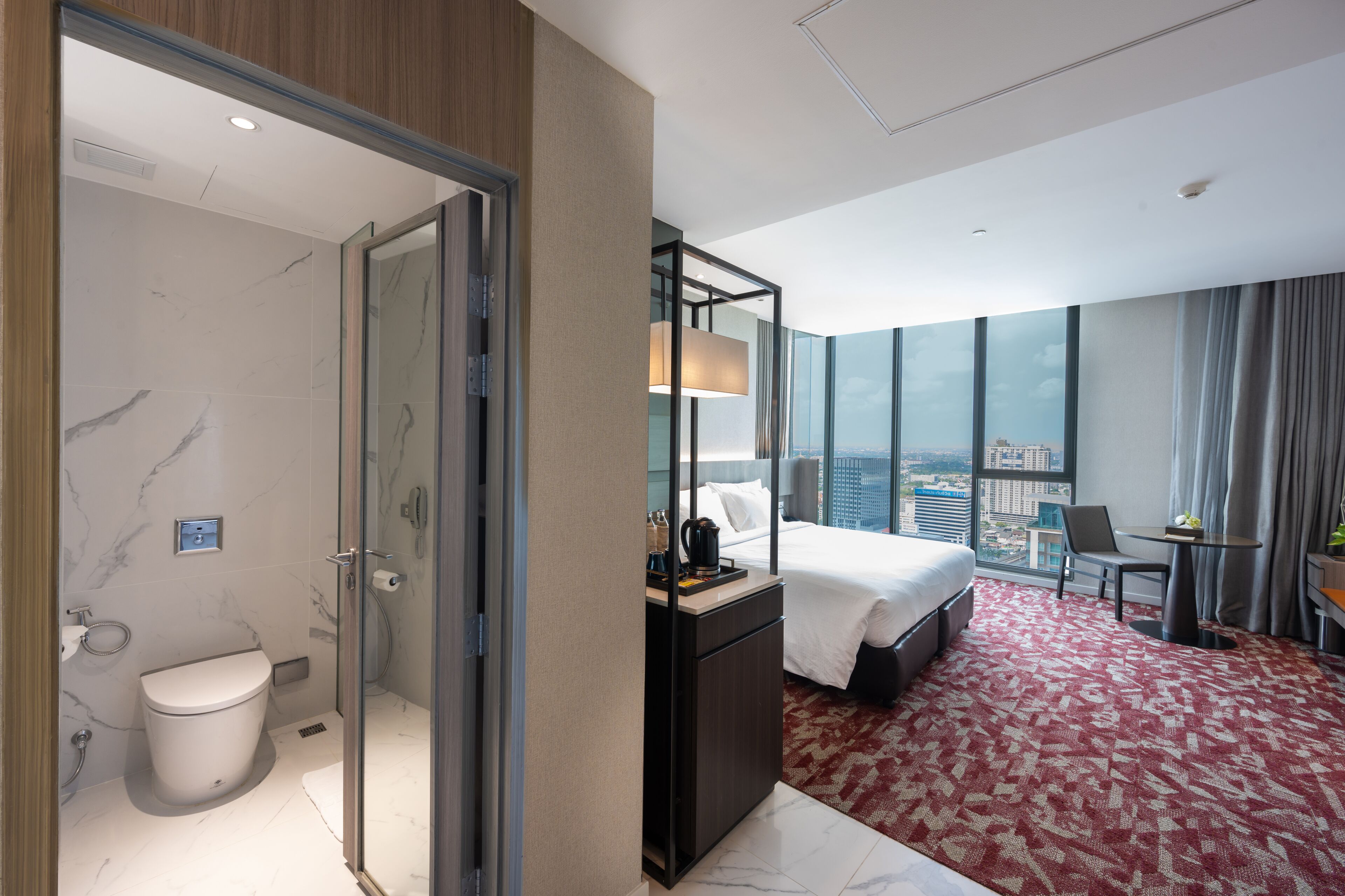 A hotel room with a bed, a desk, a chair, a bathroom with a toilet and shower, and a city view.