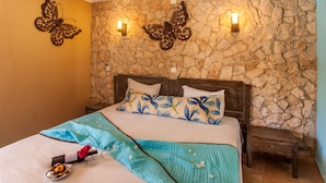Un dormitorio con pared de piedra, una cama con ropa de cama floral y dos lámparas de pared.