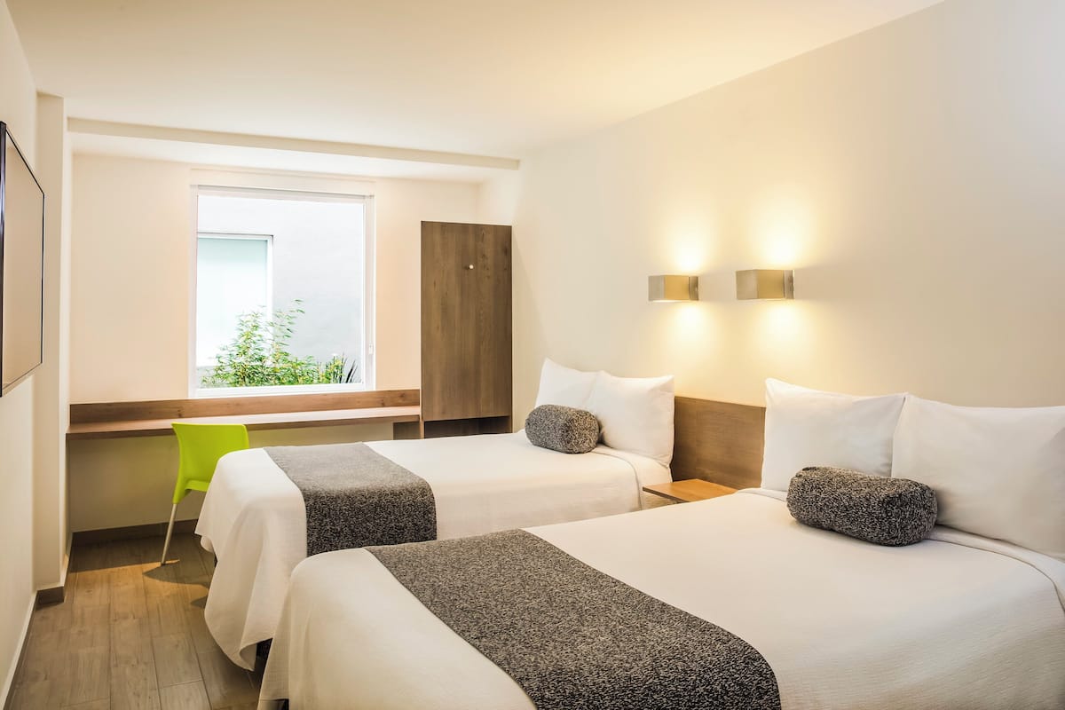 Ein Hotelzimmer mit zwei Betten, einem Fenster mit Ausblick, einem Schreibtisch und einem Stuhl.