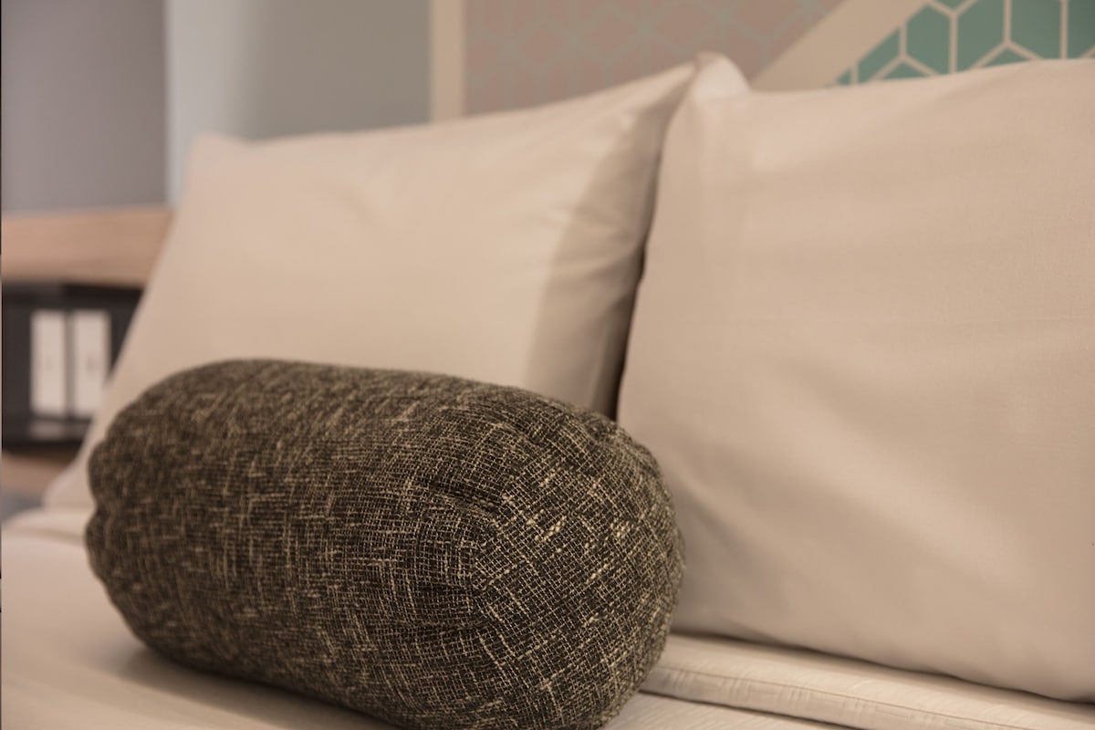 A bed with a beige pillow and a textured brown pillow.