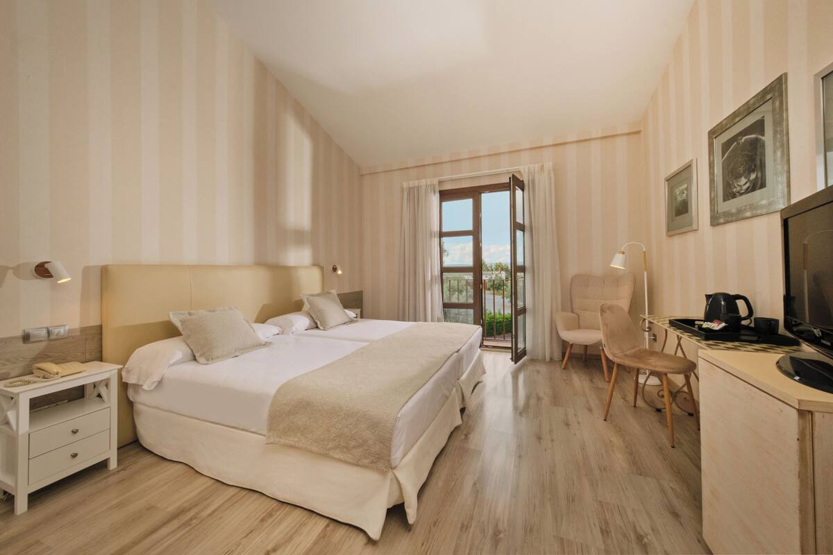 A hotel room with a large bed, a desk with a chair, a television, and a window with curtains.