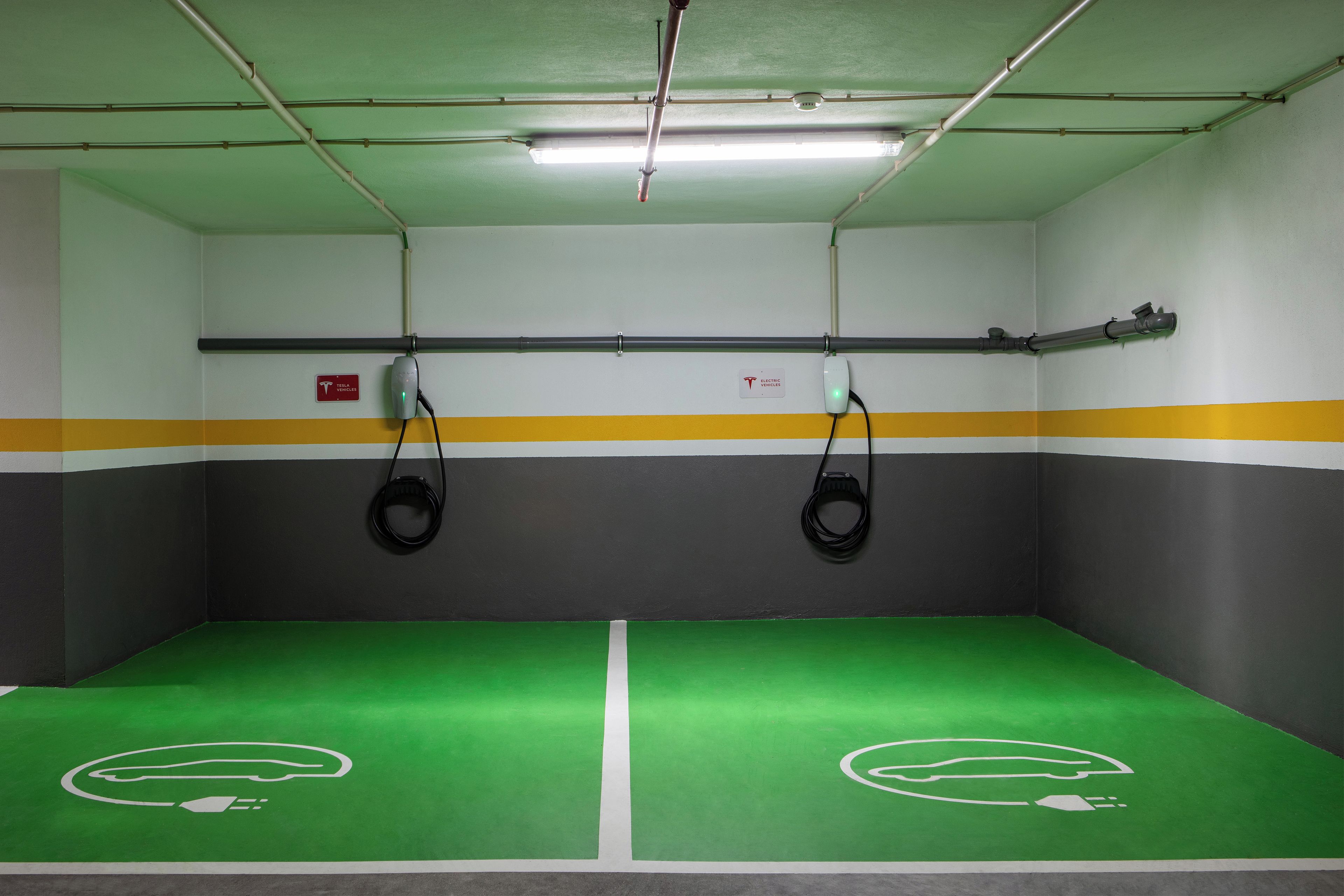 A parking garage with green and gray walls, yellow and gray stripes, and two electric vehicle charging stations.