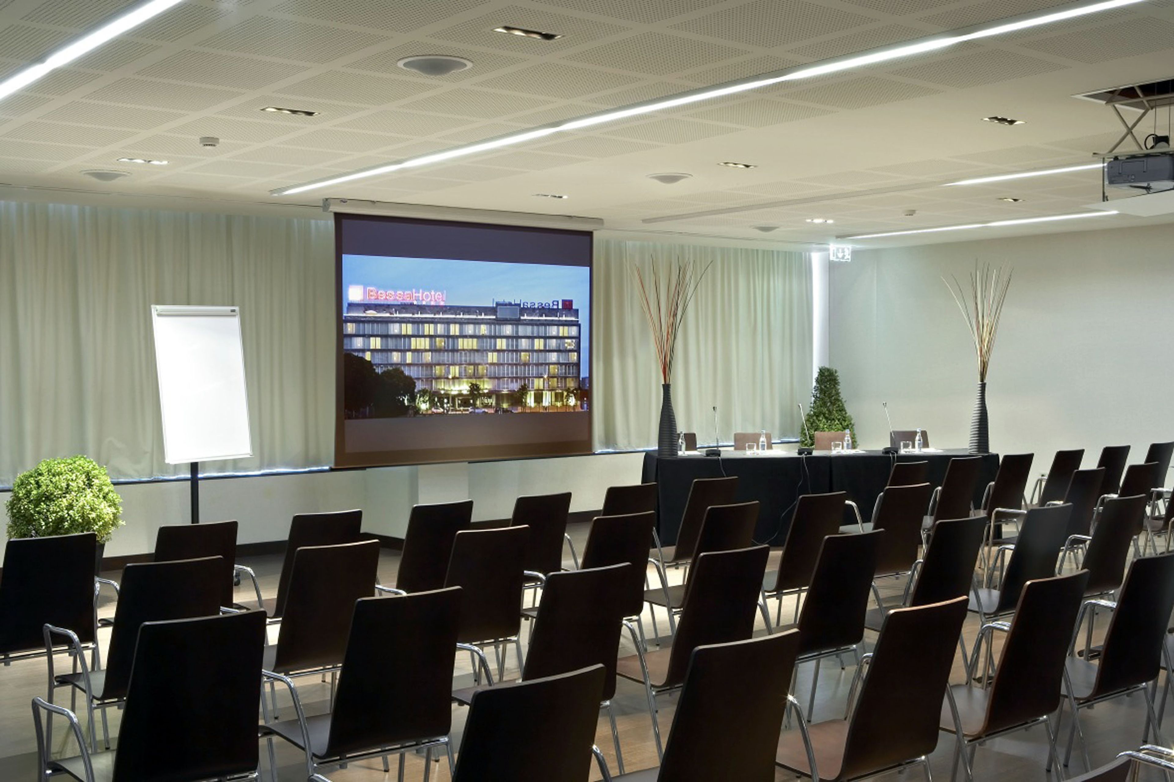 A conference room with rows of chairs facing a projection screen displaying a hotel image.