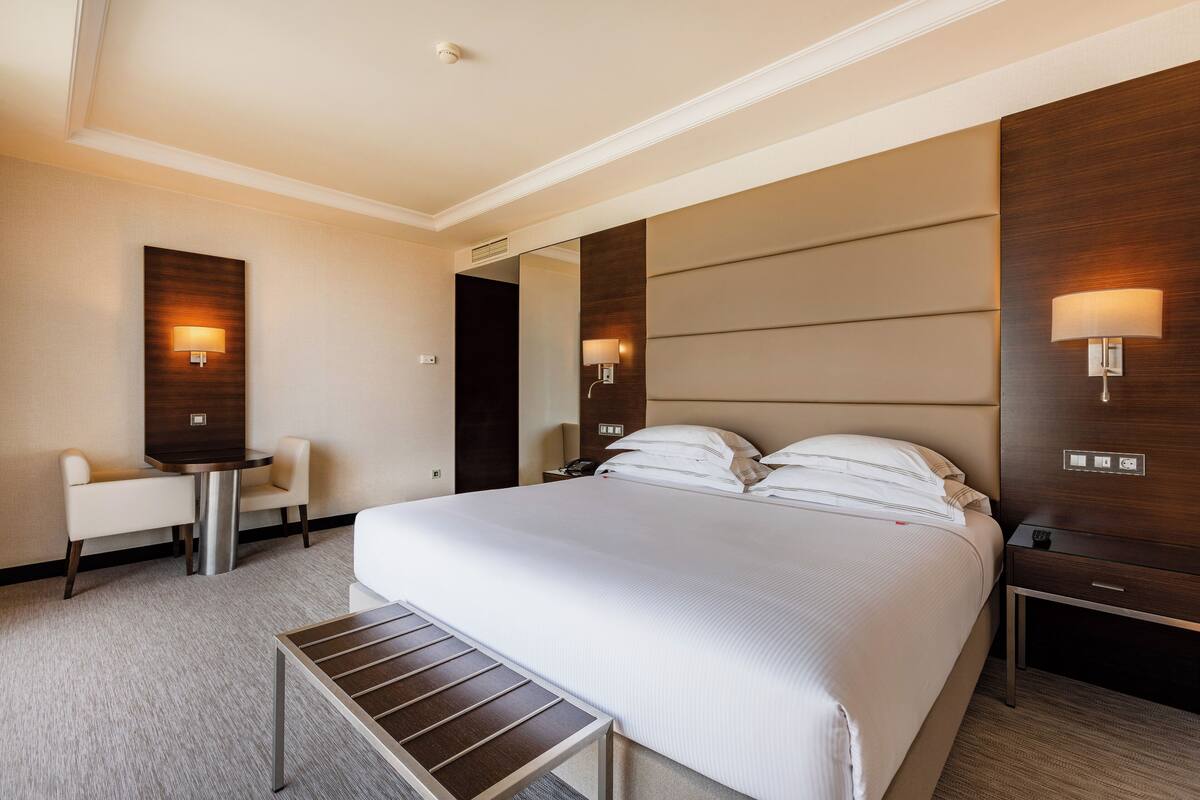 Een hotelkamer met een groot bed, een nachtkastje, een stoel, een klein tafeltje en twee wandlampen.