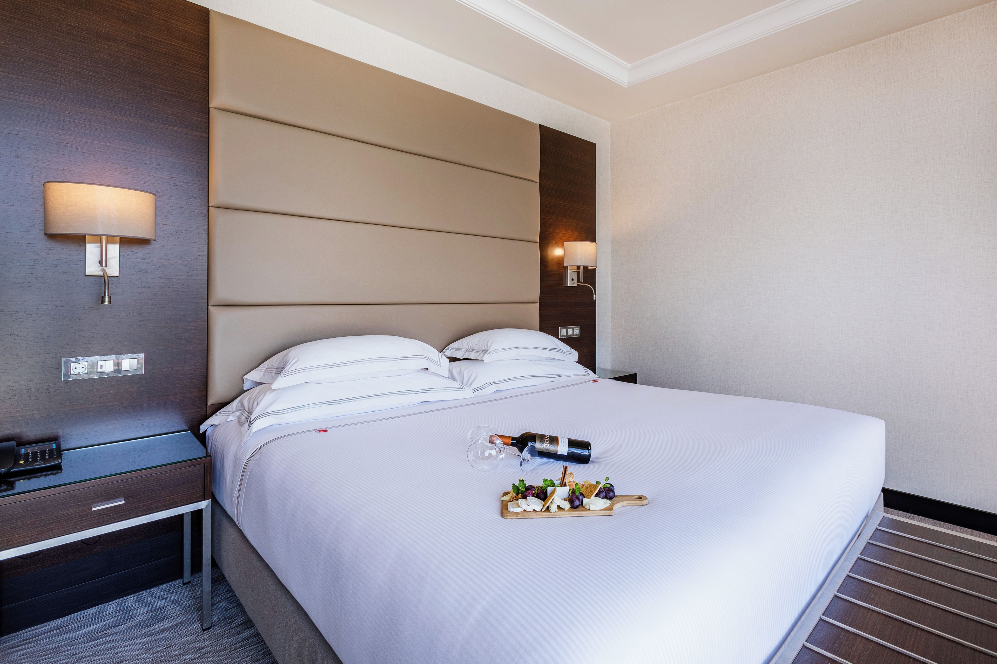 Une chambre d’hôtel avec un lit bien fait, une table de chevet avec une lampe et un plateau avec des en-cas et une bouteille.