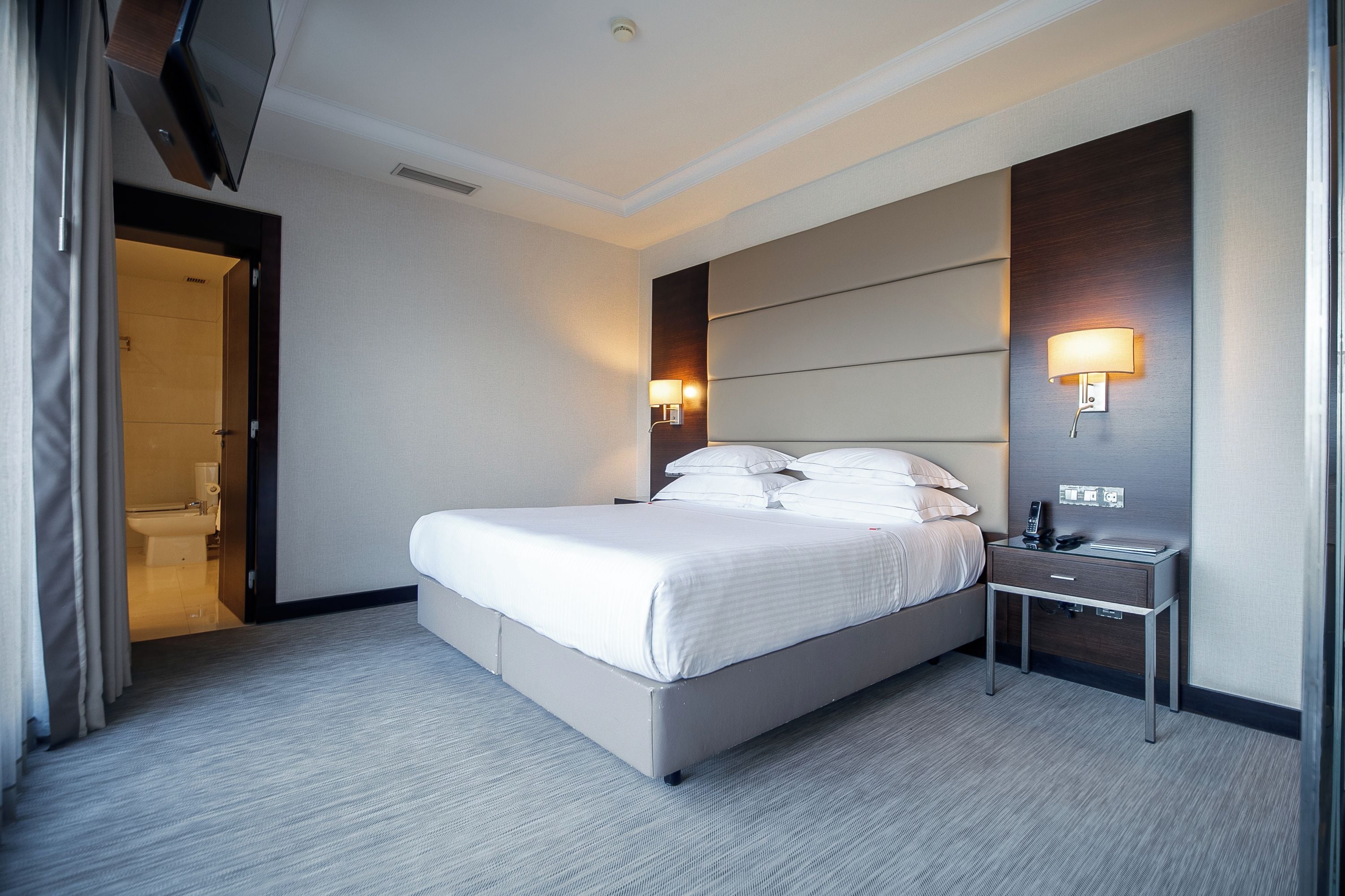Una habitación de hotel con una cama grande, una mesita de noche y una lámpara de pared.