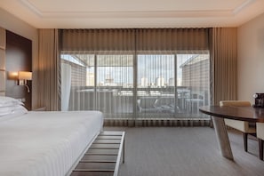 Habitación de hotel con cama, escritorio y vistas a la ciudad a través de cortinas traslúcidas.