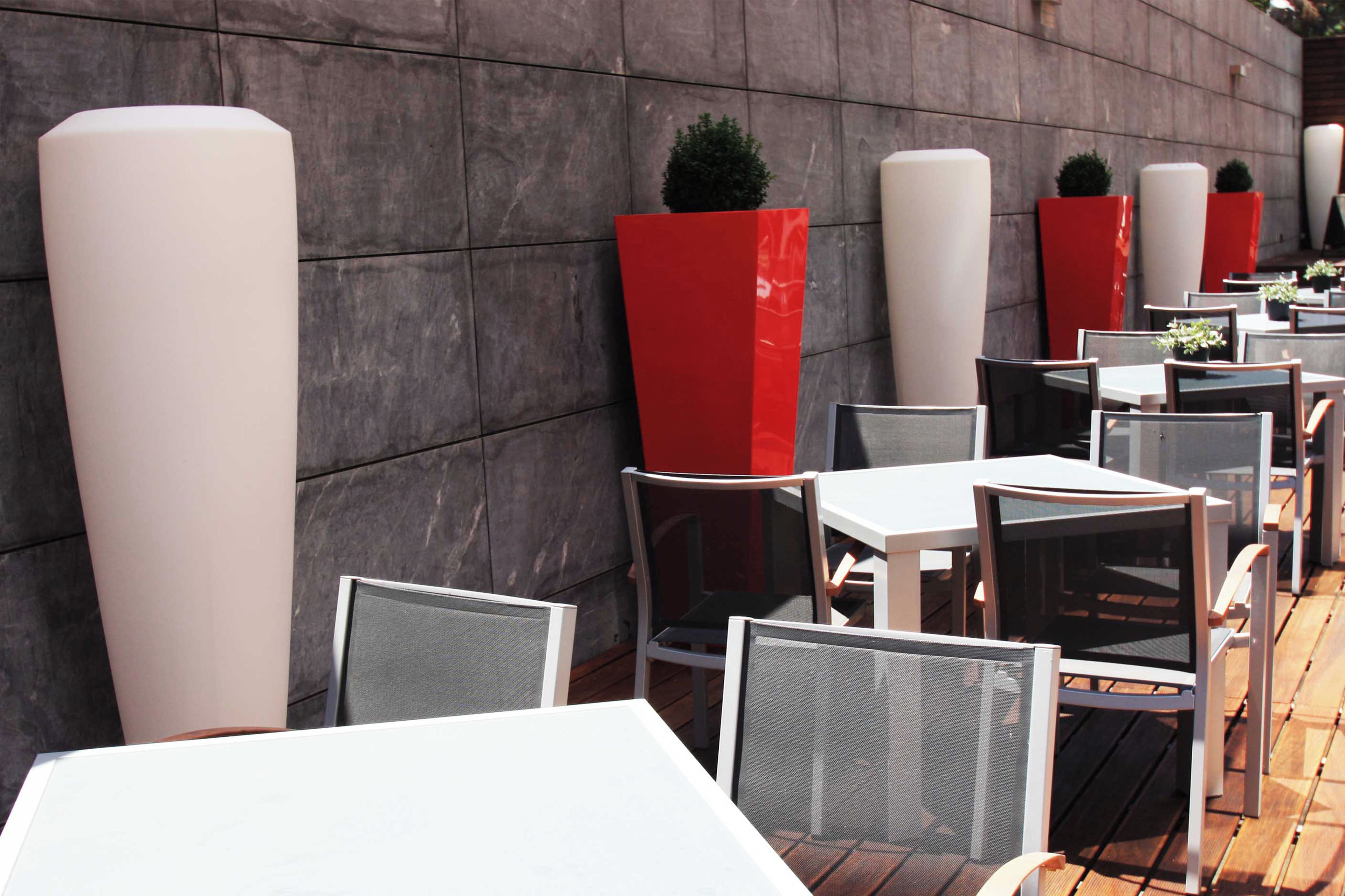 Outdoor seating with tables and chairs, red planters, and a stone wall.