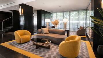 A modern lobby with a sofa set, two armchairs, a coffee table, and a staircase.