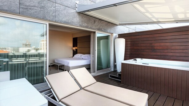 A modern outdoor lounge area with a sofa, a small table, and a hot tub. - BessaHotel Boavista (Porto)