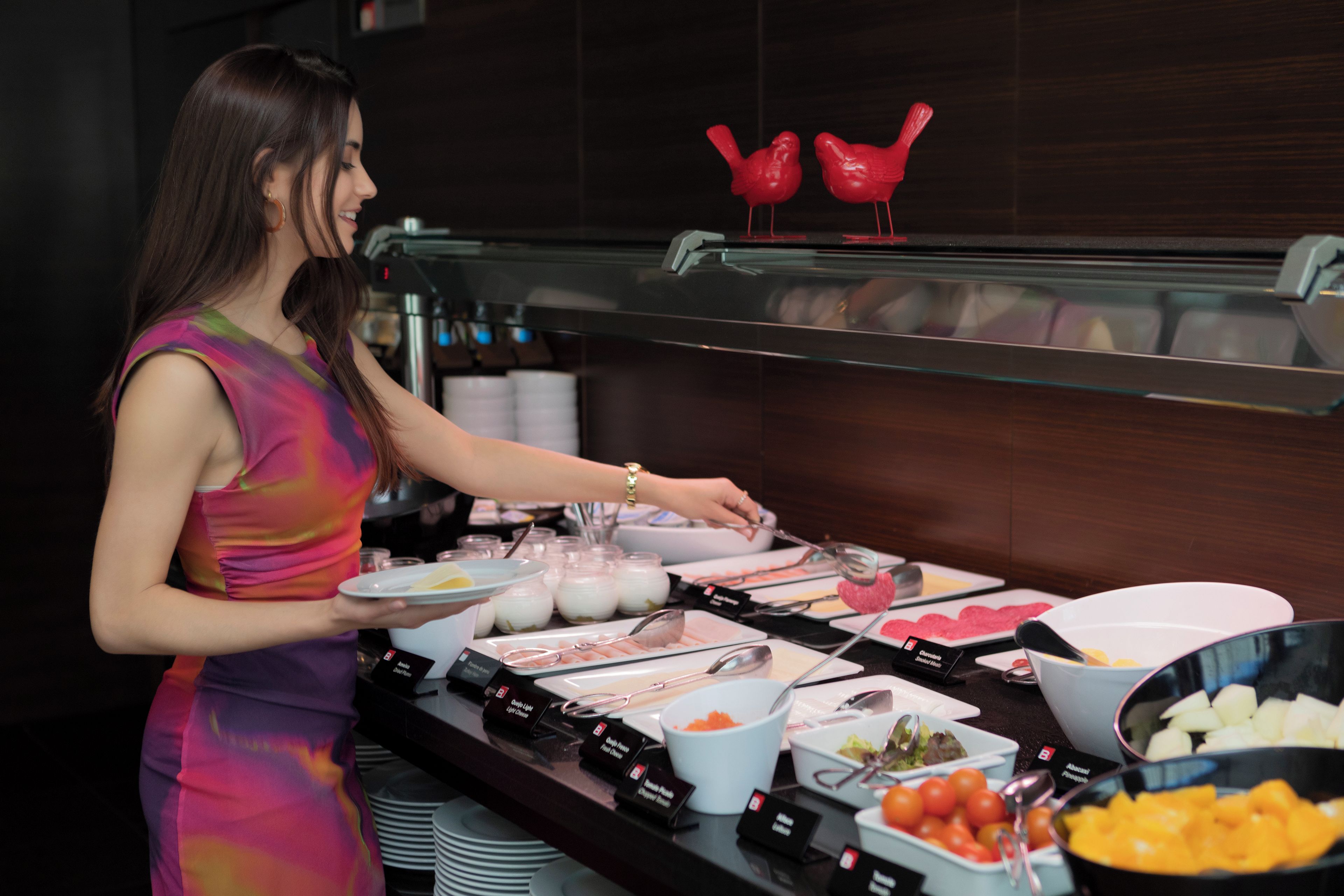Buffet com diversos alimentos e uma mulher servindo.