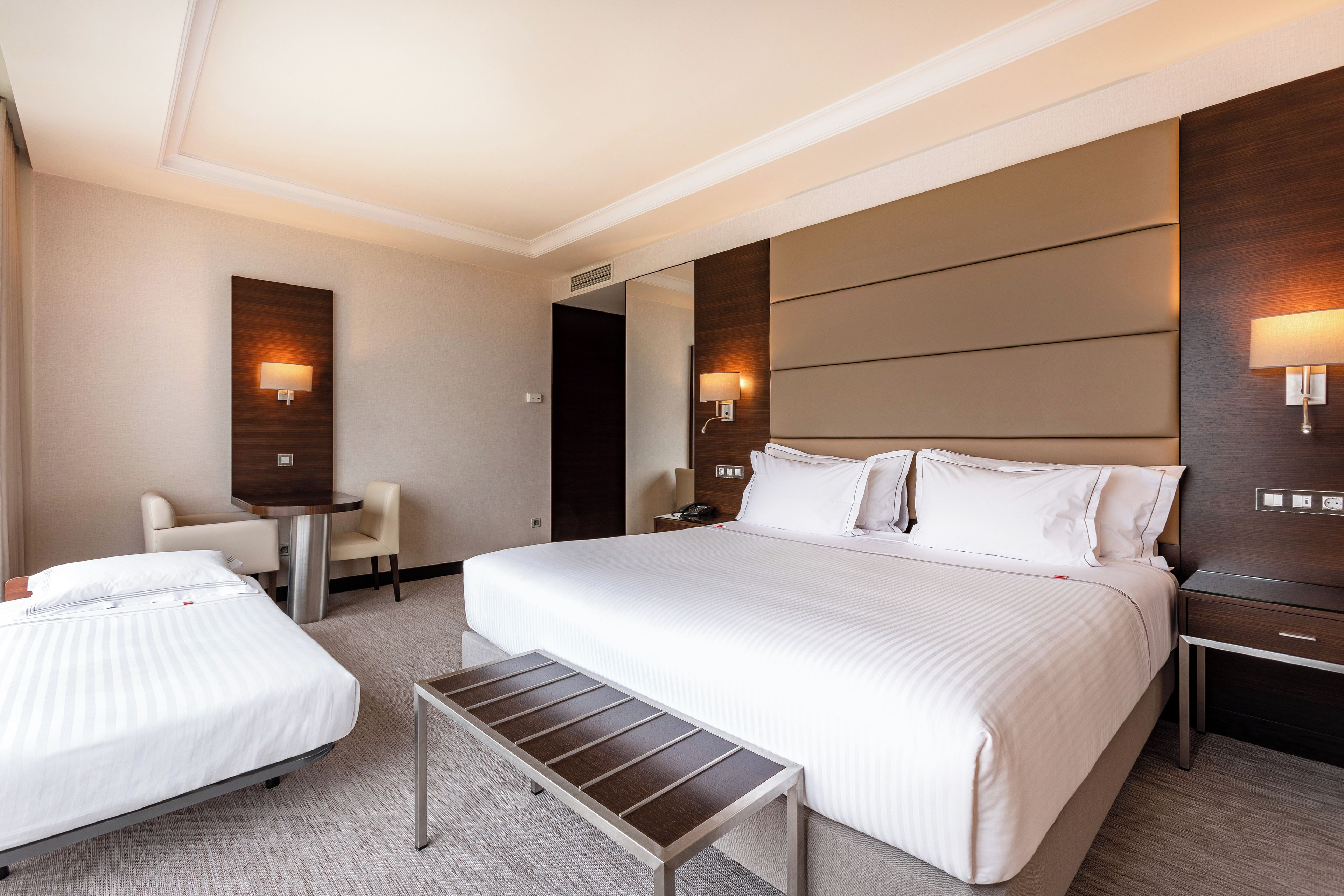 Una habitación de hotel con una cama grande, una cama más pequeña, un escritorio y dos sillas.