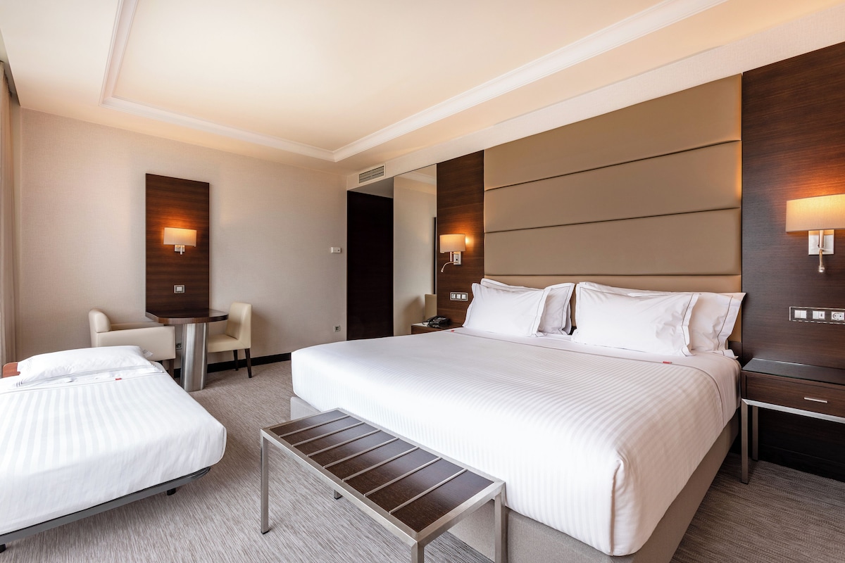 Una habitación de hotel con una cama grande, una cama más pequeña, un escritorio y dos sillas.